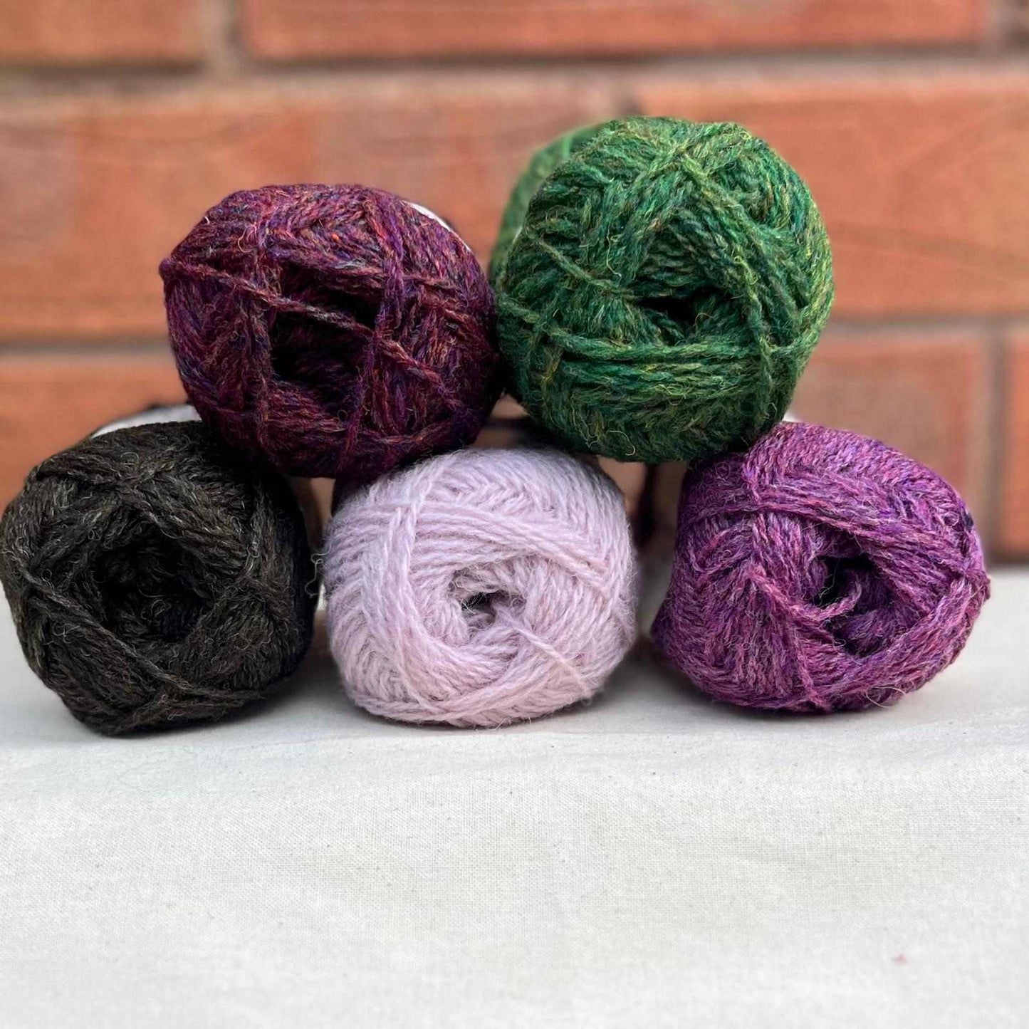 5 balls of yarn in shades of black, pink and green