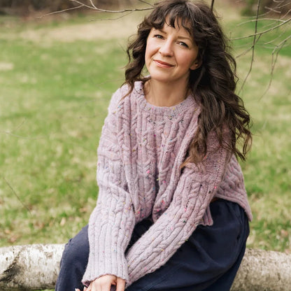 Woman sitting on a log in a natural setting wearing a pink sweater.