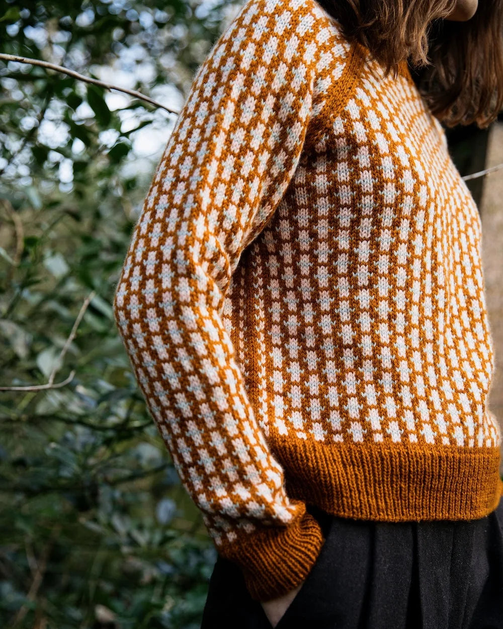 Person wearing a patterned sweater with blurred greenery in the background